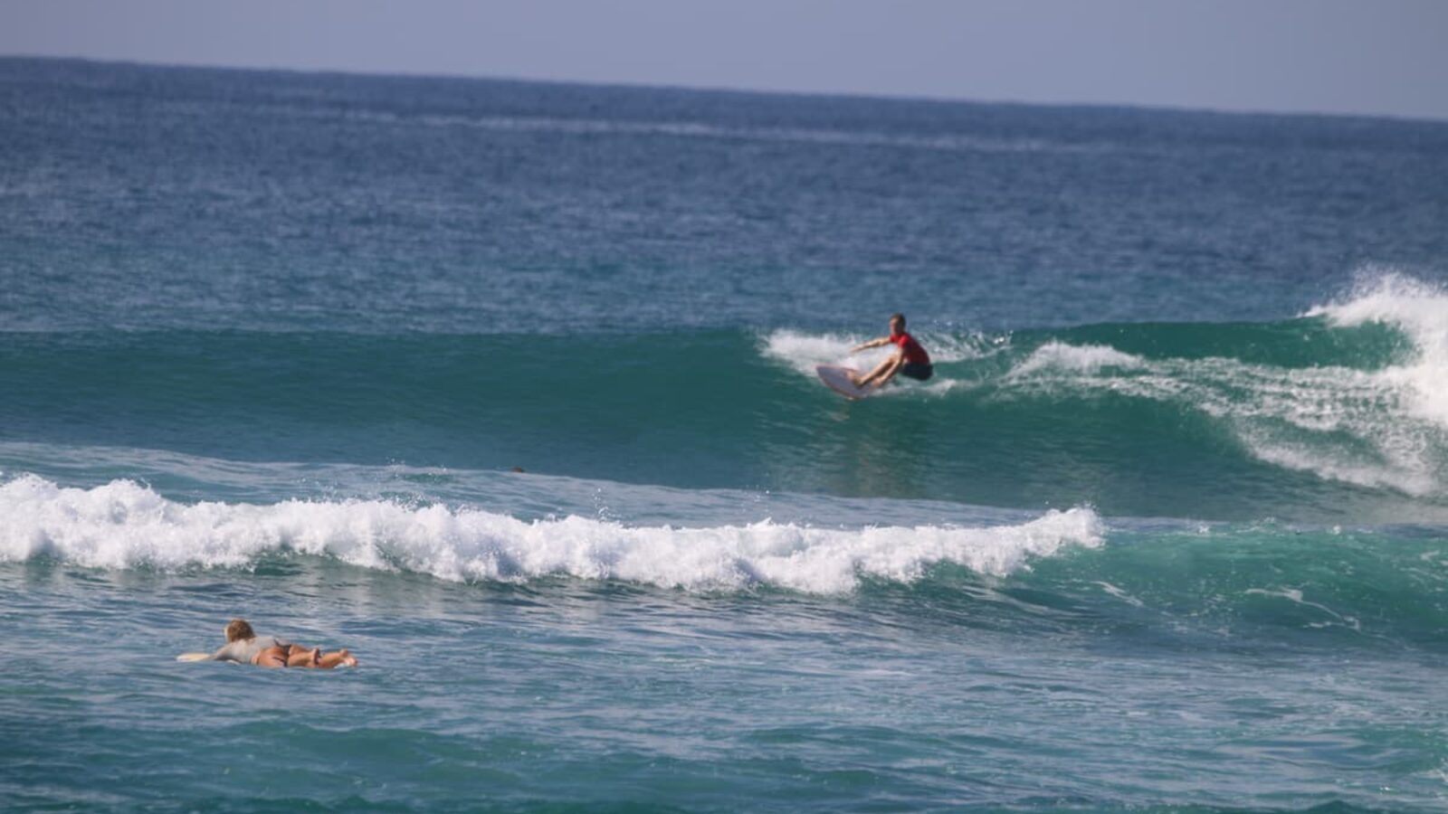 A surfer trimming across a clean open face with another paddling out